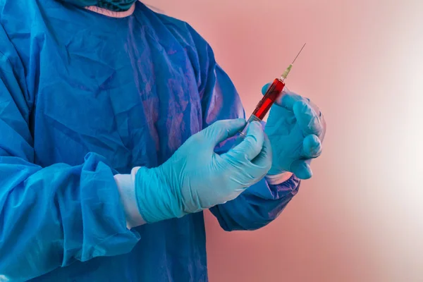 Doctor with gloves and protective equipment prepares a syringe with red medicine