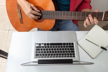 Sanal bir ders sırasında klasik bir gitar ve dizüstü bilgisayarın detaylarının havadan çekilmiş görüntüsü. Karantina sırasında etkinlikler