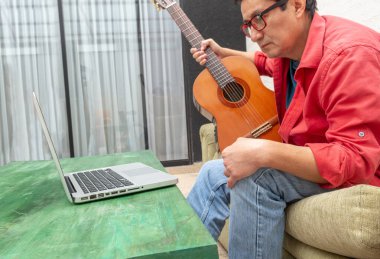Çevrimiçi öğrenme kavramı. Genç adam evdeki dizüstü bilgisayarı sayesinde gitar çalmayı öğrenirken konsantre oluyor..
