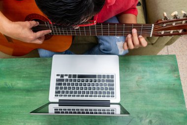 Karantinası sırasında evde online gitar dersi alan bir adamın hava görüntüsü.