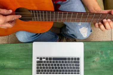 Bilgisayarının önünde duran birinin belinin görüntüsü. Evden internet üzerinden gitar dersleri alıyor.