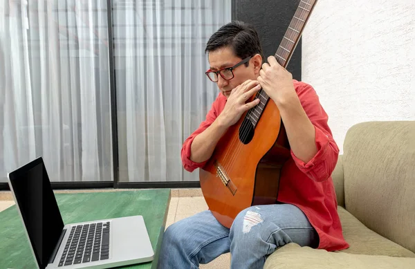 Evinin oturma odasında, bir adam bilgisayarına yakından bakar ve sanal gitar dersi alır.