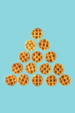Uçan yiyecekler piramidi ya da modaya uygun mavi arka planda izole edilmiş küçük yuvarlak waffle yığınları. Asgari gıda ve fırın konsepti, modern ve çağdaş tarz, kapat