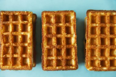 Moda mavisi arka planda üç Belçika waffle 'ı. Asgari gıda ve fırın konsepti, modern ve çağdaş tarz, üst görünüm ve kapatma