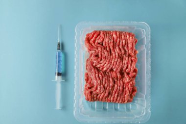 İçinde mavi sıvı protein, antibiyotik, hormonlar veya diğer kimyasal ve biyolojik katkı maddeleri olan öğütülmüş et ve şırınga. Yapay et konsepti. Geleceğin gıdası, üst görünüm, düzlük