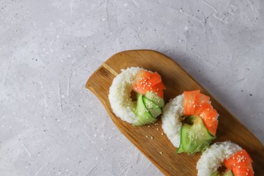 Çiğ havuç ve salatalıklı vejetaryen suşi çörekleri. Tahta tahtada vejetaryen pirinç simidi. Gri beton arka planda moda Japon yemekleri, yakın plan.