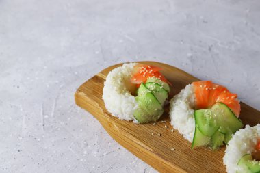 Çiğ havuç ve salatalıklı vejetaryen suşi çörekleri. Tahta tahtada vejetaryen pirinç simidi. Gri beton arka planda moda Japon yemekleri, yakın plan.