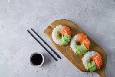 Çiğ havuçlu ve salatalıklı suşi çörekleri. Tahta tahtada soya soslu vejetaryen pirinç simidi. Gri beton arka planda moda Japon yemekleri, üst manzara, düz yatış