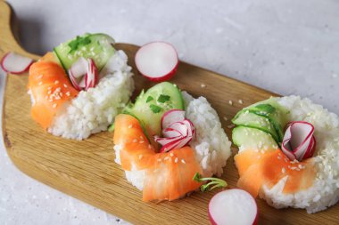 Çiğ havuçlu, turplu ve salatalıklı vejetaryen suşi çörekleri. Tahta tahtada vejetaryen pirinç simidi. Gri beton arka planda moda Japon yemekleri, yakın plan.