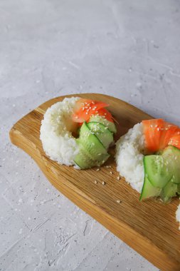 Çiğ havuç ve salatalıklı vejetaryen suşi çörekleri. Tahta tahtada vejetaryen pirinç simidi. Gri beton arka planda moda Japon yemekleri, yakın plan.