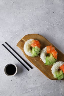 Çiğ havuçlu ve salatalıklı suşi çörekleri. Tahta tahtada soya soslu vejetaryen pirinç simidi. Gri beton arka planda moda Japon yemekleri, üst manzara, düz yatış