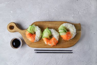 Çiğ havuçlu ve salatalıklı suşi çörekleri. Tahta tahtada soya soslu vejetaryen pirinç simidi. Gri beton arka planda moda Japon yemekleri, üst manzara, düz yatış