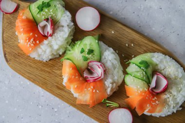 Çiğ havuçlu, turplu ve salatalıklı vejetaryen suşi çörekleri. Tahta tahtada vejetaryen pirinç simidi. Gri beton arka planda moda Japon yemekleri, yakın plan.