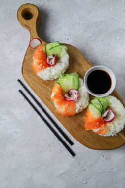 Çiğ havuçlu, turplu ve salatalıklı vejetaryen suşi çörekleri. Tahta tahtada vejetaryen pirinç simidi. Gri beton arka planda moda Japon yemekleri, yakın plan, üst manzara