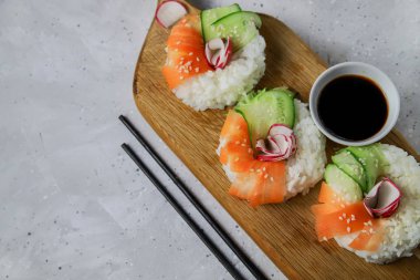Çiğ havuçlu, turplu ve salatalıklı vejetaryen suşi çörekleri. Tahta tahtada vejetaryen pirinç simidi. Gri beton arka planda moda Japon yemekleri, yakın plan, üst manzara