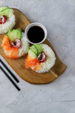 Çiğ havuçlu, turplu ve salatalıklı vejetaryen suşi çörekleri. Tahta tahtada vejetaryen pirinç simidi. Gri beton arka planda moda Japon yemekleri, yakın plan, üst manzara