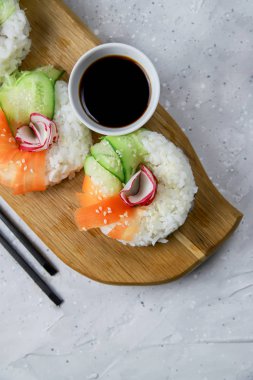 Çiğ havuçlu, turplu ve salatalıklı vejetaryen suşi çörekleri. Tahta tahtada vejetaryen pirinç simidi. Gri beton arka planda moda Japon yemekleri, yakın plan, üst manzara