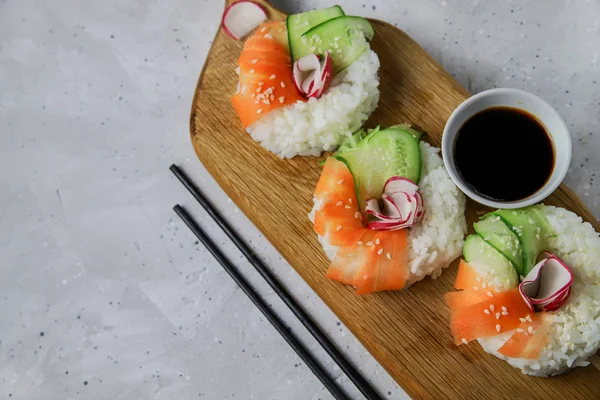 Çiğ havuçlu, turplu ve salatalıklı vejetaryen suşi çörekleri. Tahta tahtada vejetaryen pirinç simidi. Gri beton arka planda moda Japon yemekleri, yakın plan, üst manzara