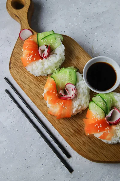 Çiğ havuçlu, turplu ve salatalıklı vejetaryen suşi çörekleri. Tahta tahtada vejetaryen pirinç simidi. Gri beton arka planda moda Japon yemekleri, yakın plan, üst manzara