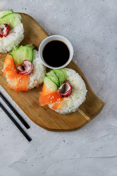 Çiğ havuçlu, turplu ve salatalıklı vejetaryen suşi çörekleri. Tahta tahtada vejetaryen pirinç simidi. Gri beton arka planda moda Japon yemekleri, yakın plan, üst manzara
