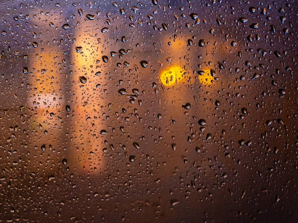 As luzes da cidade noturna durante a chuva atrás de um copo coberto com gotas de água. Abstrato desfocado fundo . — Fotografia de Stock