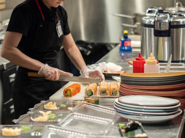 Hands in latex gloves cut the rolls with a large knife. Traditional Japanese food made from rice and salmon.