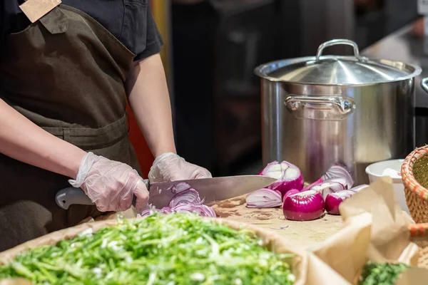 Руки повара в целлофановых перчатках режут красный лук тонкими ломтиками. Приготовление овощей . — стоковое фото