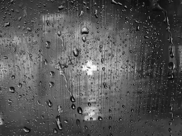 A visão de uma cruz médica brilhando no escuro na farmácia através do vidro enevoado, como a última esperança de salvação. Fundo de vidro preto e branco com gotas de chuva fluindo para baixo . — Fotografia de Stock