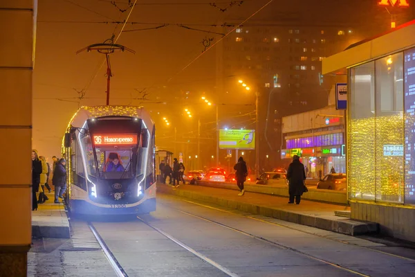 Moscow.Russia. December 26, 2019. Trams in the fog lit by a network of LEDs arrive at a bus stop with passengers. Environmentally friendly public transport, decorated in honor of the New Year holidays — Stock Photo, Image