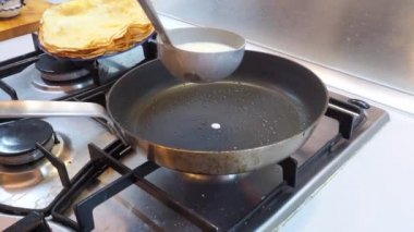 Bir el, hamuru kızgın bir tavaya metal bir kovayla dolduruyor. Ev yapımı nefis kokulu krep pişirme süreci..