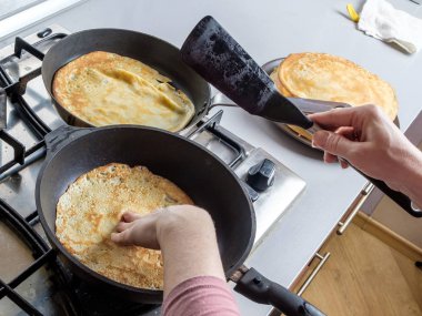 İnsan eli spatula tutarken tavada krep pişirir. Ev mutfağı. Maslenitsa bayramı için geleneksel ziyafet.