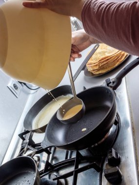 Hamur, metal bir kovadan kızgın bir tavaya dökülüyor. Krep pişirme süreci.