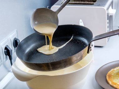 Hamur, metal bir kovadan kızgın bir tavaya dökülüyor. Krep pişirme süreci.