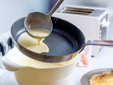 Hamur, metal bir kovadan kızgın bir tavaya dökülüyor. Krep pişirme süreci.