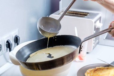 Hamur, metal bir kovadan kızgın bir tavaya dökülüyor. Krep pişirme süreci.