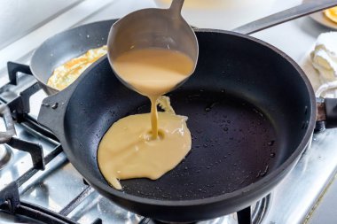 Hamur, metal bir kovadan kızgın bir tavaya dökülüyor. Krep pişirme süreci.