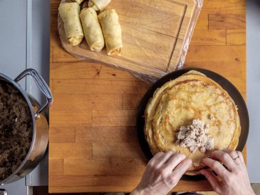 İnsan elinin üst görüntüsü ahşap bir arka planda taze pişmiş krep dolduruyor.. 