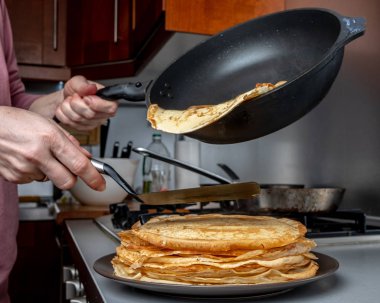İnsan eli spatula tutuyor ve tava sıcak krepi tabağa yayıyor buharın geldiği tabağa. Ev mutfağı. 