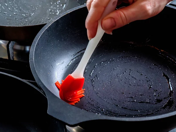 Рука людини змащує червону гарячу сковороду червоним силіконовим кухонним пензлем. Готуємося випікати млинці на домашній кухні . — стокове фото