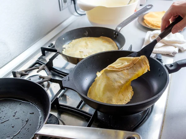 Руки людини з кухонним шпателем перевертають гарячий ароматний млинчик на сковороді під час процесу випічки. Домашня кухня . — стокове фото