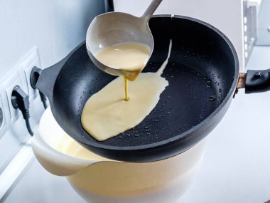 Hamur, metal bir kovadan kızgın bir tavaya dökülüyor. Krep pişirme süreci.