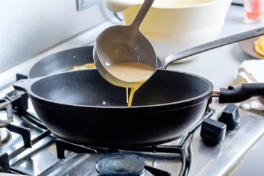 Hamur, metal bir kovadan kızgın bir tavaya dökülüyor. Krep pişirme süreci.