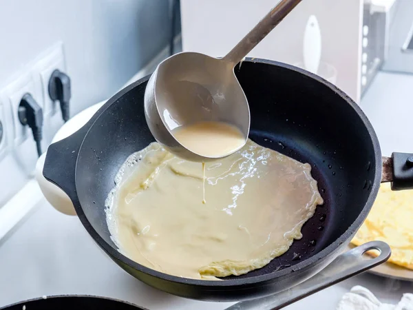 Баттер виливається з металевого відра на змащену сковороду. Процес випічки млинців . — стокове фото