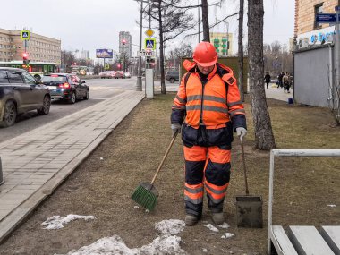 Moskova, Rusya. 26 Şubat 2020. Turuncu elbiseli bir kamu görevlisi ve bir kask bulutlu bir sabahta şehir bölgesini temizliyor. Elinde bir süpürge ve faraş var..