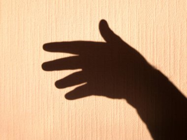 Parlak ışıkla aydınlatılmış sarı bir duvardaki insan avucunun gölgesi. Parmaklarla hareket et.