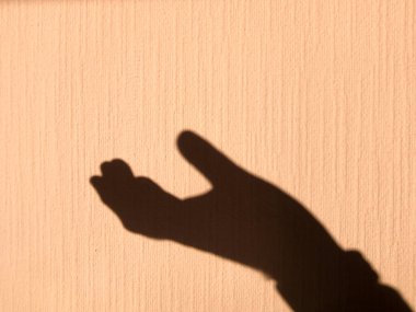 Parlak ışıkla aydınlatılmış sarı bir duvarda insan avucunun gölgesi. Dilekçenin ifadesi.