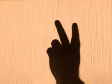 Sarı, parlak bir duvarda insan elinin gölgesi var. Zafer ve mükemmelliği simgeleyen iki parmağın kaldırılışı..