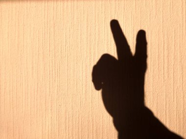 Sarı, parlak bir duvarda insan elinin gölgesi var. Zafer ve mükemmelliği simgeleyen iki parmağın kaldırılışı..