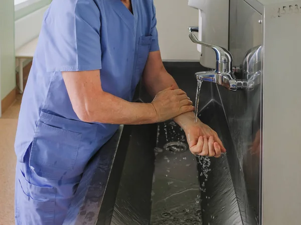 A surgeon washes his hands under a faucet in a stainless steel wash-hand basin. Preparing for a surgical operation. Dysenfection and sterilization.