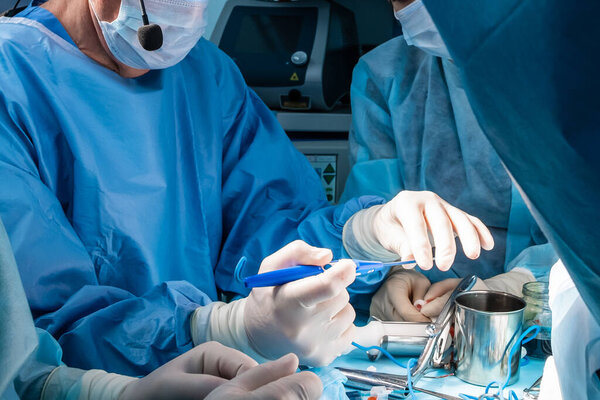 A group of surgeons performing minimally invasive surgery on the patient's anus using surgical instruments. Surgeons have sterile blue surgical clothing.